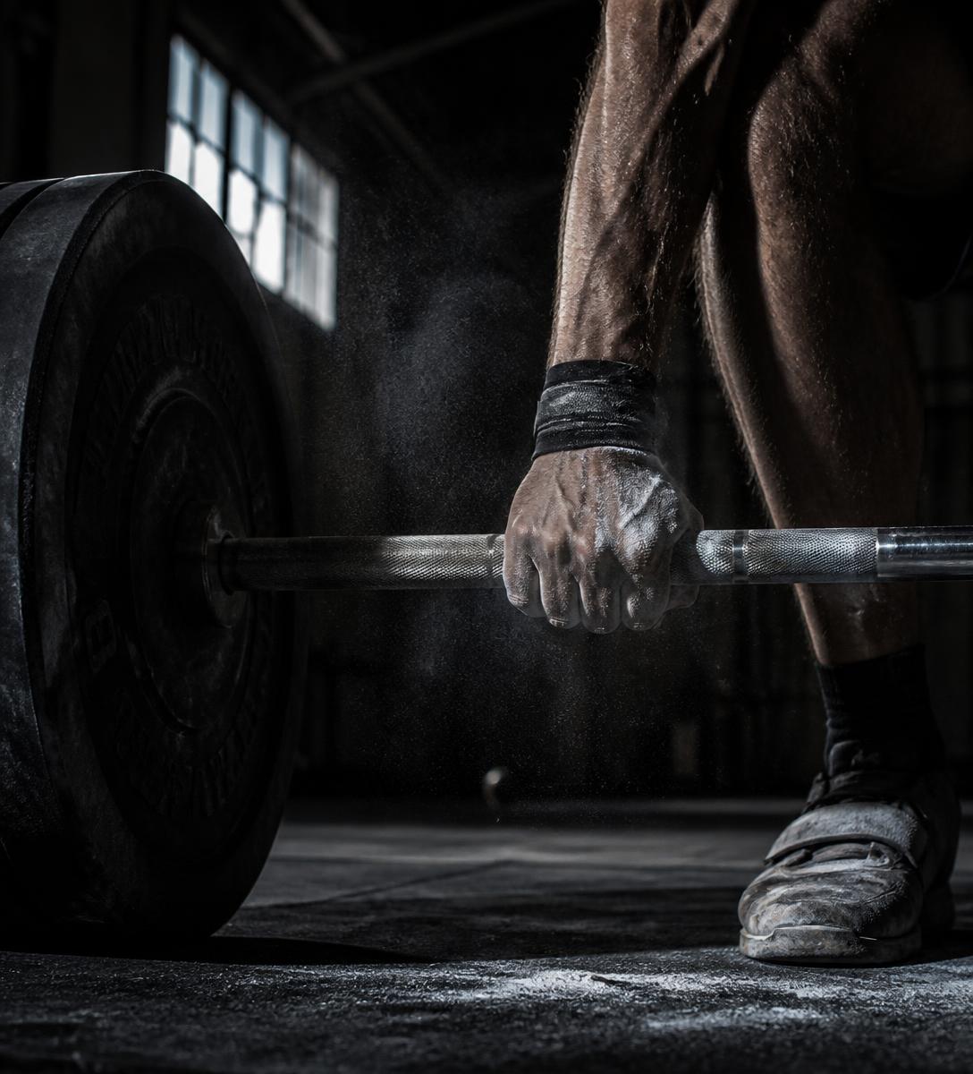 Chalked hand gripping a loaded barbell in a dark industrial gym